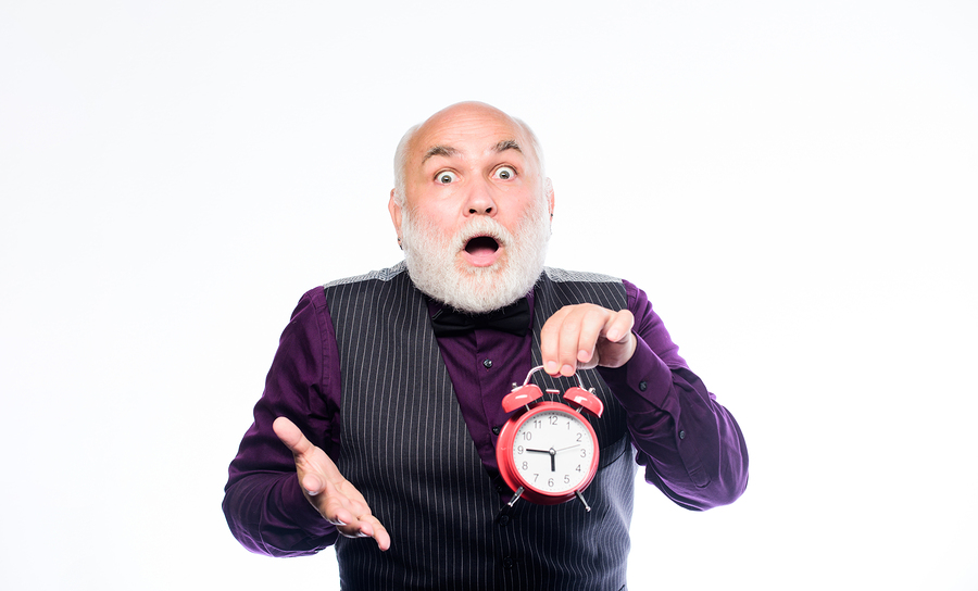 Older gentleman holding an analogue clock with a shocked expression on his face.