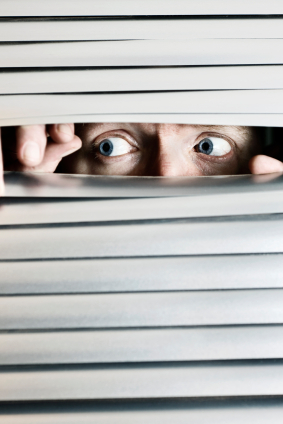 Person looking out from behind closed blinds, afraid