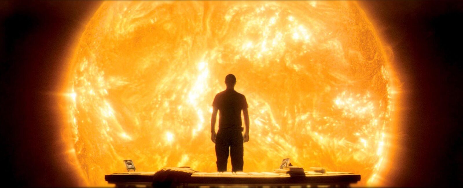 Still from the movie "Sunshine". The character Searle (played by Cliff Curtis) stands with a bench behind him. In front of him is the swirling sun, dimmed but occupying his entire field of vision.