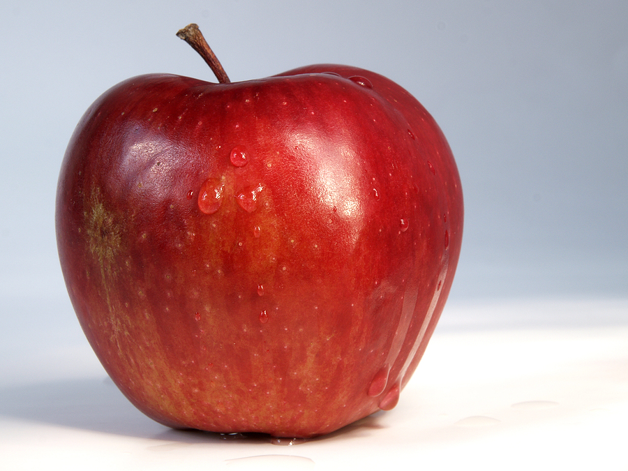 Red apple sitting on a white surface with a stalk coming out of the top/centre.